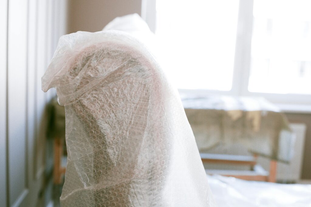 pexels-photo-3616736-3616736 Furniture wrapped in bubble wrap for protection during a move in a bright sunlit room.
